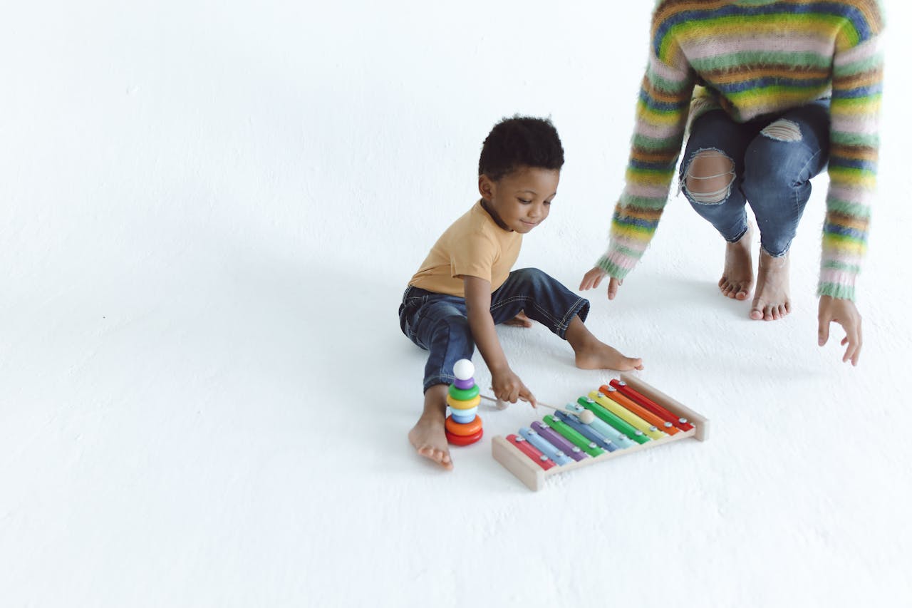 Services Young child playing with a colorful xylophone indoors, supervised by an adult.