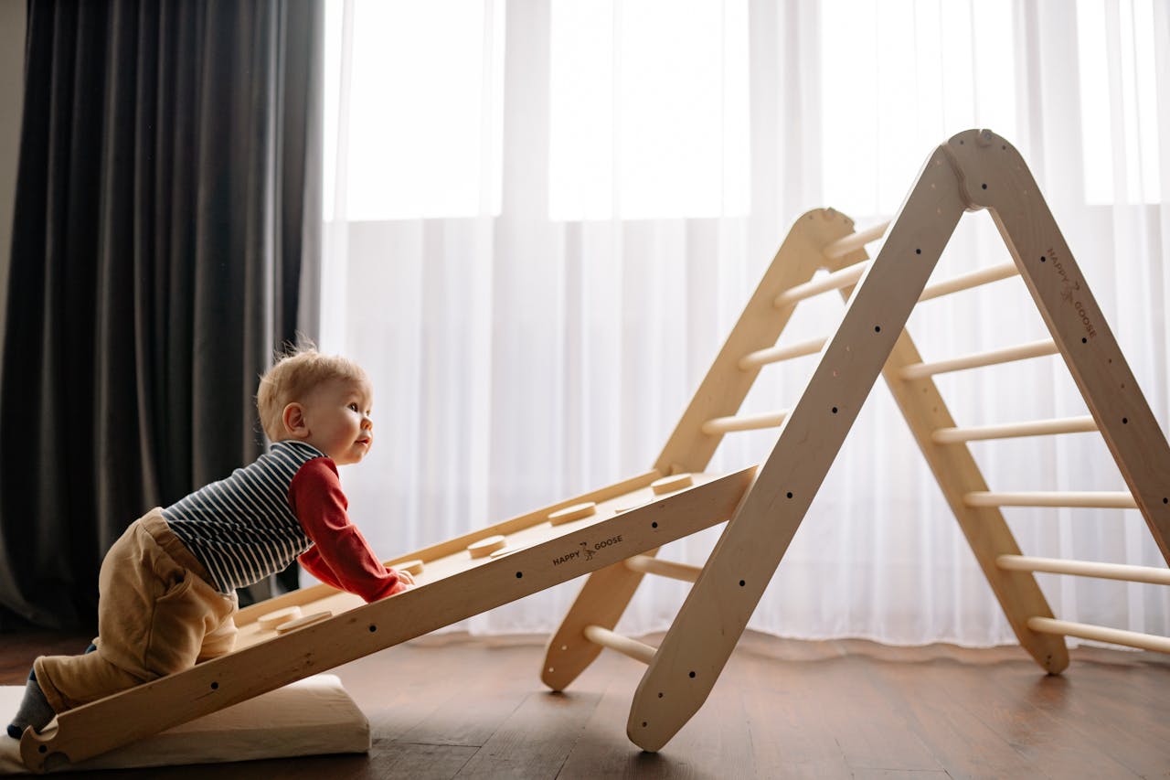 Home A baby joyfully climbs a wooden play structure inside a well-lit room.